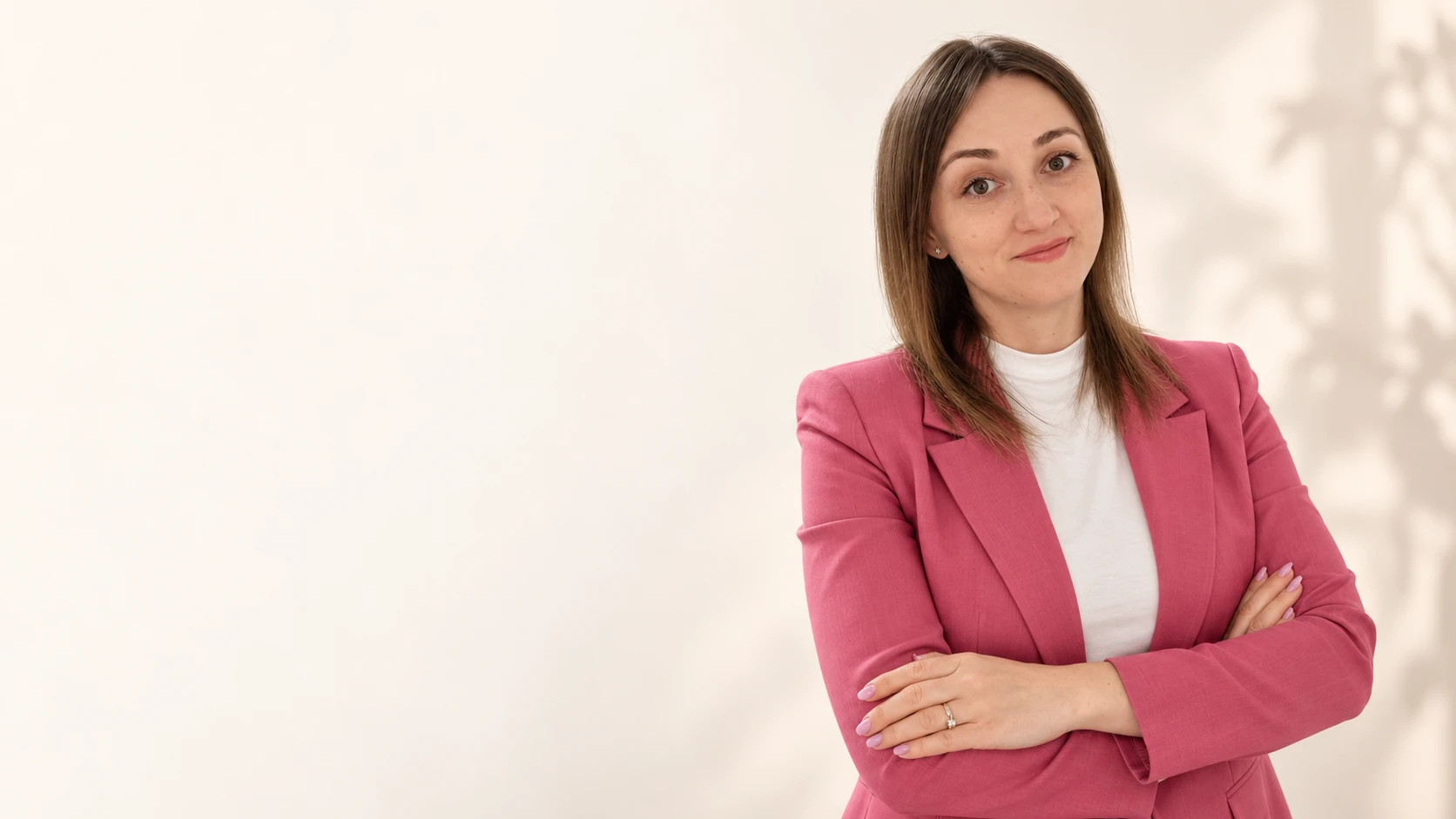 Melania Popa în sacou roz, cu brațele încrucișate, pe un fundal crem luminos.