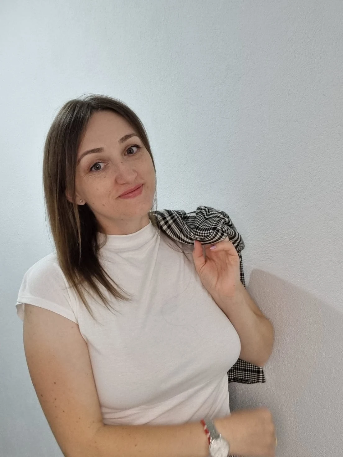 Melania Popa, în tricou alb, ținând sacoul în carouri pe umăr.