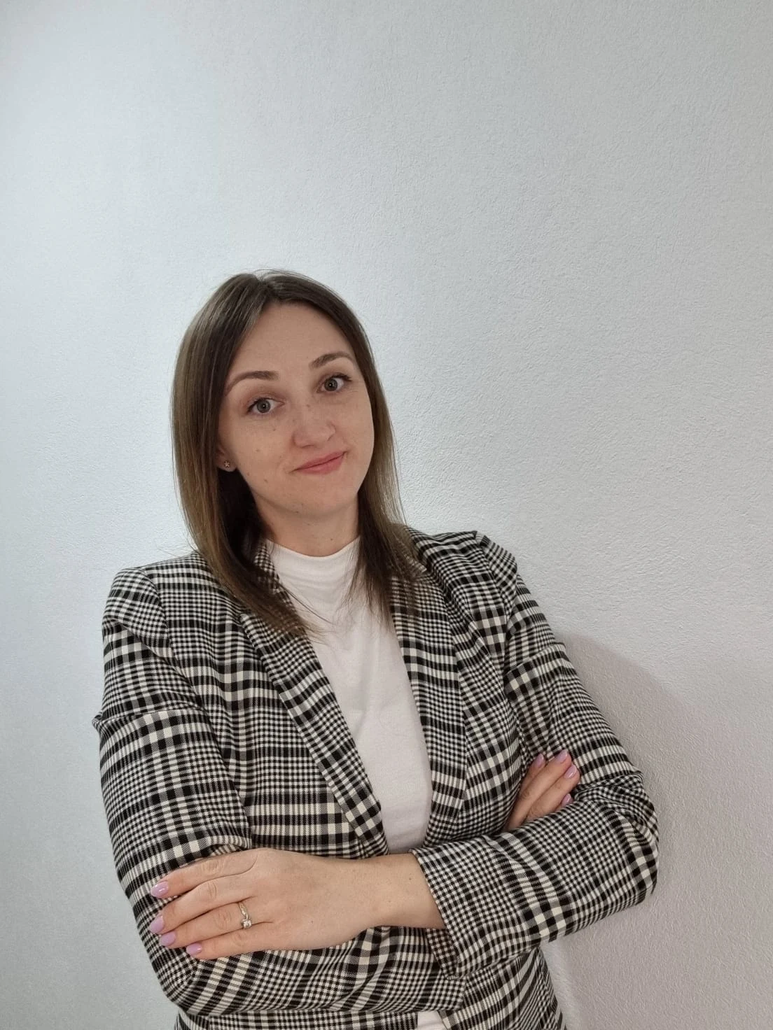 Melania Popa în sacou în carouri, cu brațele încrucișate, pe un fundal luminos.